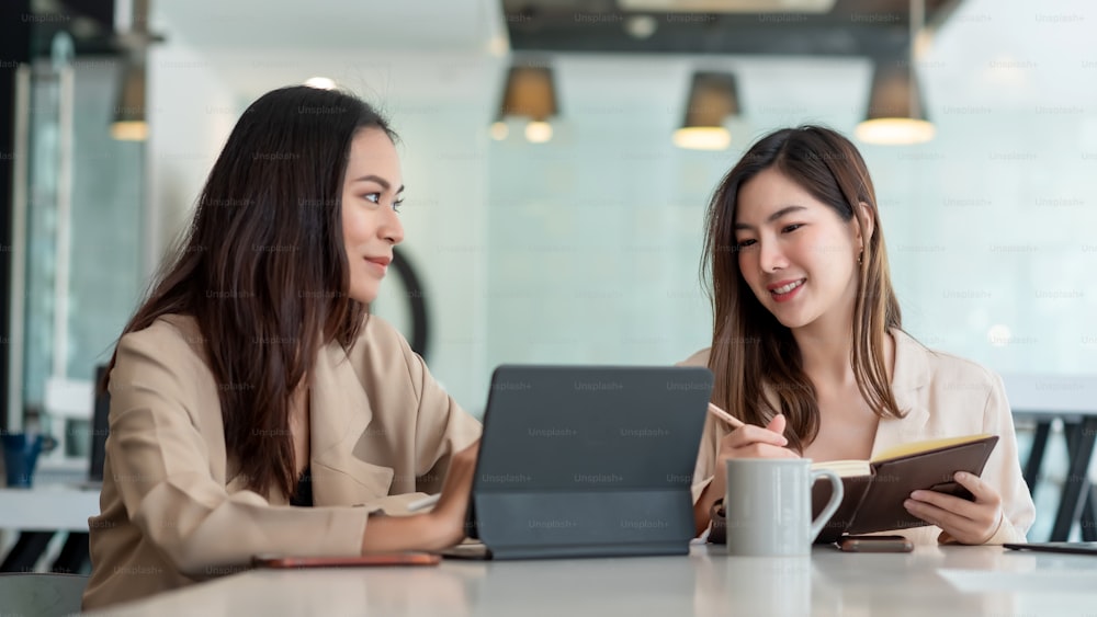 Duas jovens empresárias asiáticas estão felizes trabalhando em apresentações usando papéis e tablet colocados no escritório.