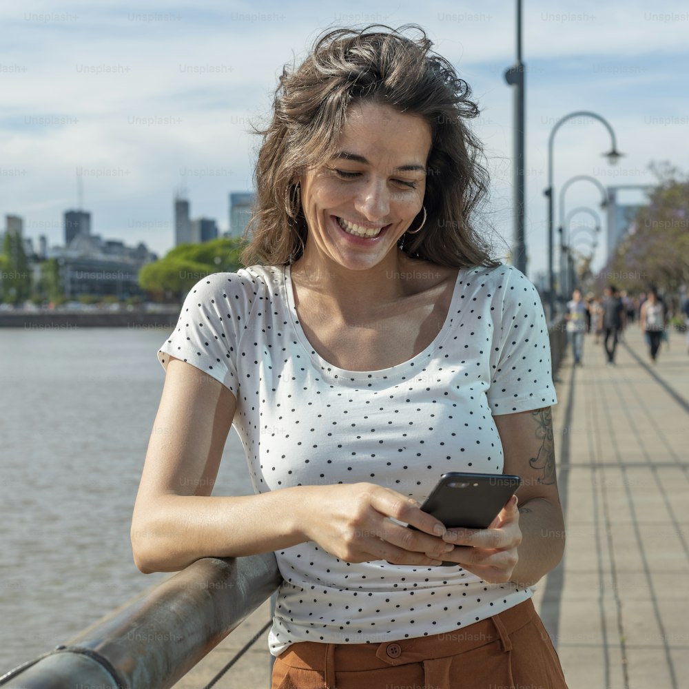 Uma jovem mulher sorridente enviando mensagens de texto ao telefone em Puerto Madero, Buenos Aires