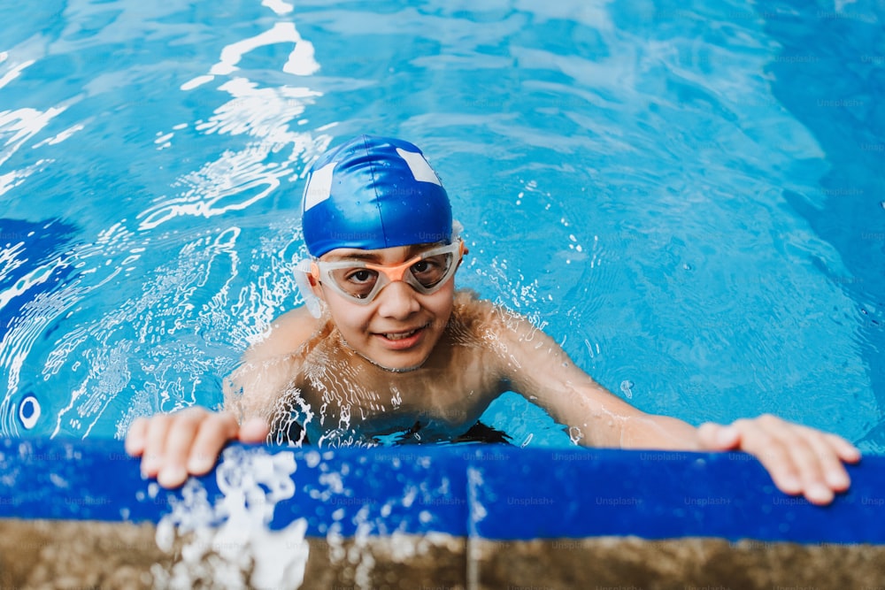 ラテンアメリカのプールで水泳のトレーニングで帽子とゴーグルを身に着けているラテンチャイルドの男の子の水泳選手