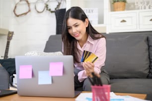 Una giovane bella donna sta usando la carta di credito per lo shopping online sul sito web di Internet a casa, concetto di e-commerce