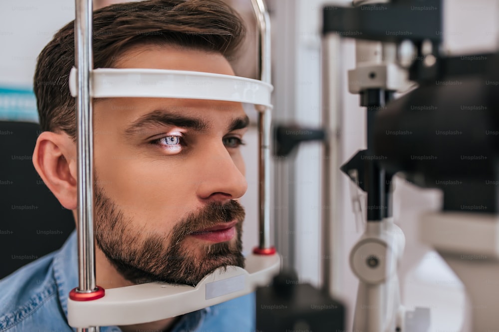 Ein gutaussehender junger Mann überprüft das Sehvermögen in einer modernen Augenklinik. Patient in Augenklinik