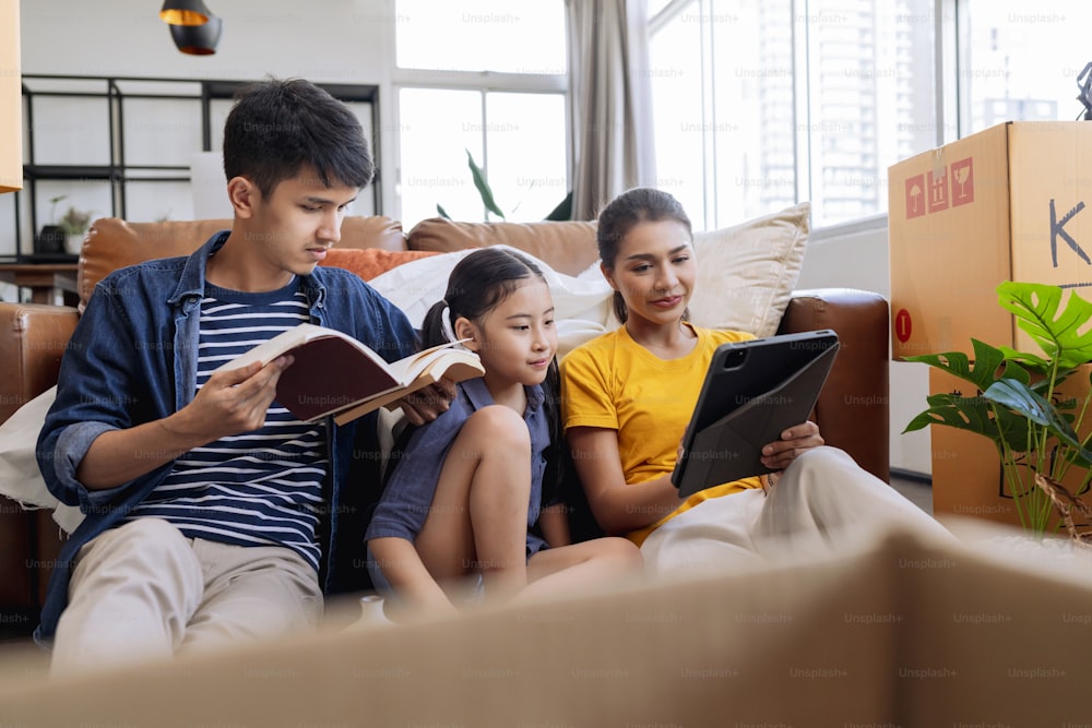 moving home concept,asian family relax leisure time sit together with cardboard box and stuff,dad mom  daughter spending time together after finish packing stuff furniture for home apartment moving