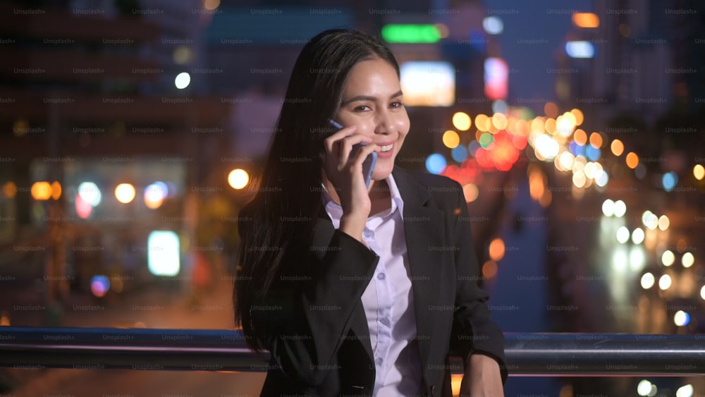 A young beautiful business woman is using smart phone in city over traffic lights at evening. business and technology concept.
