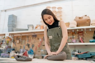 Asian Young woman female artist wear apron making clay vase bowl Beautiful young sculptor creates a clay art vase in home studio warehouse,Ceramist artist female hand warm up massage dirt clay