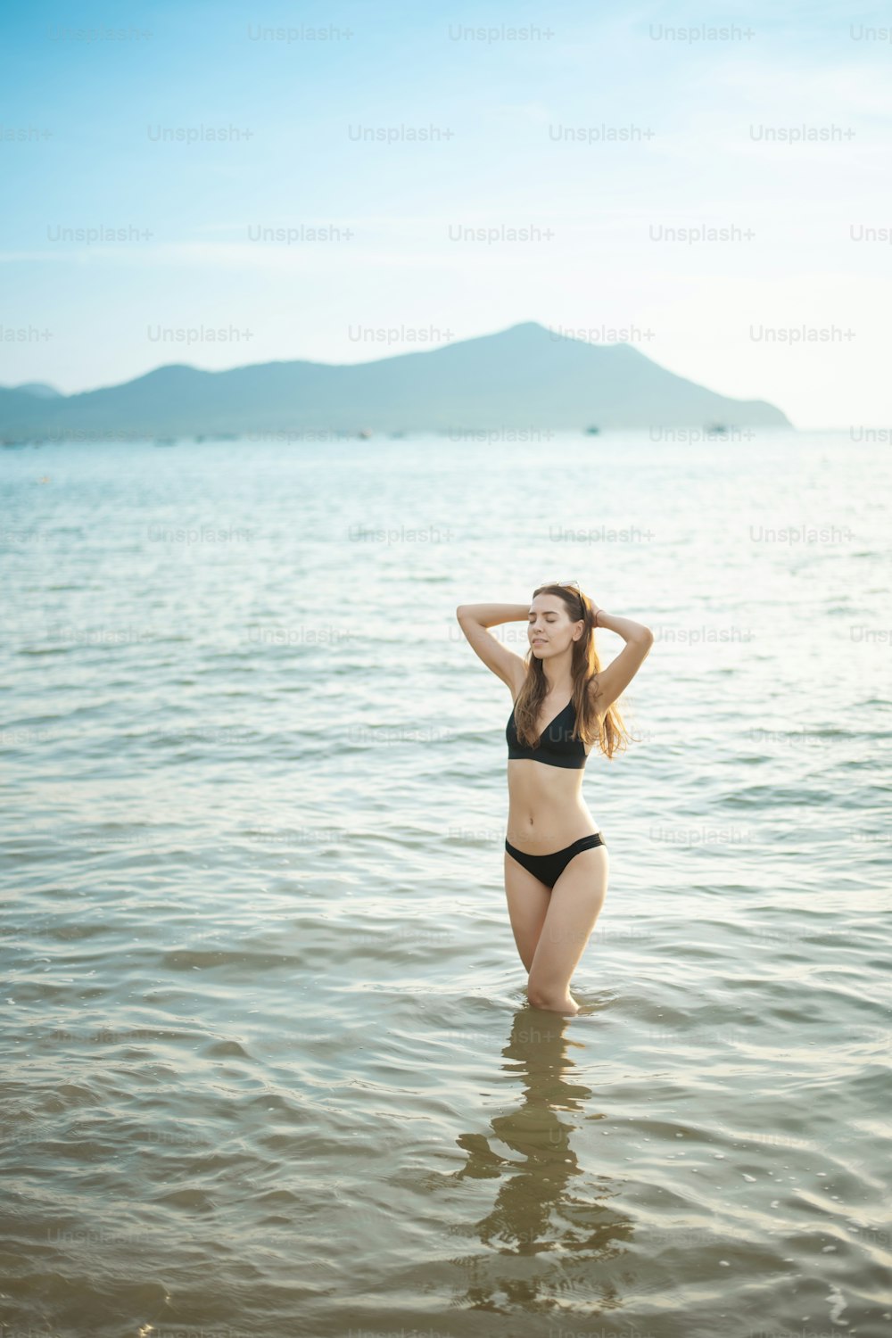Schöne Frau im schwarzen Bikini genießt mit Meerwasser am Strand