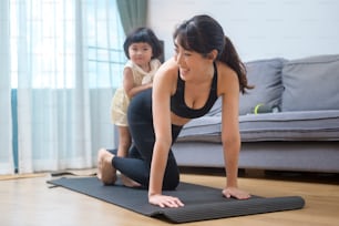 A happy young woman in sportswear is with daughter exercising in living room at home