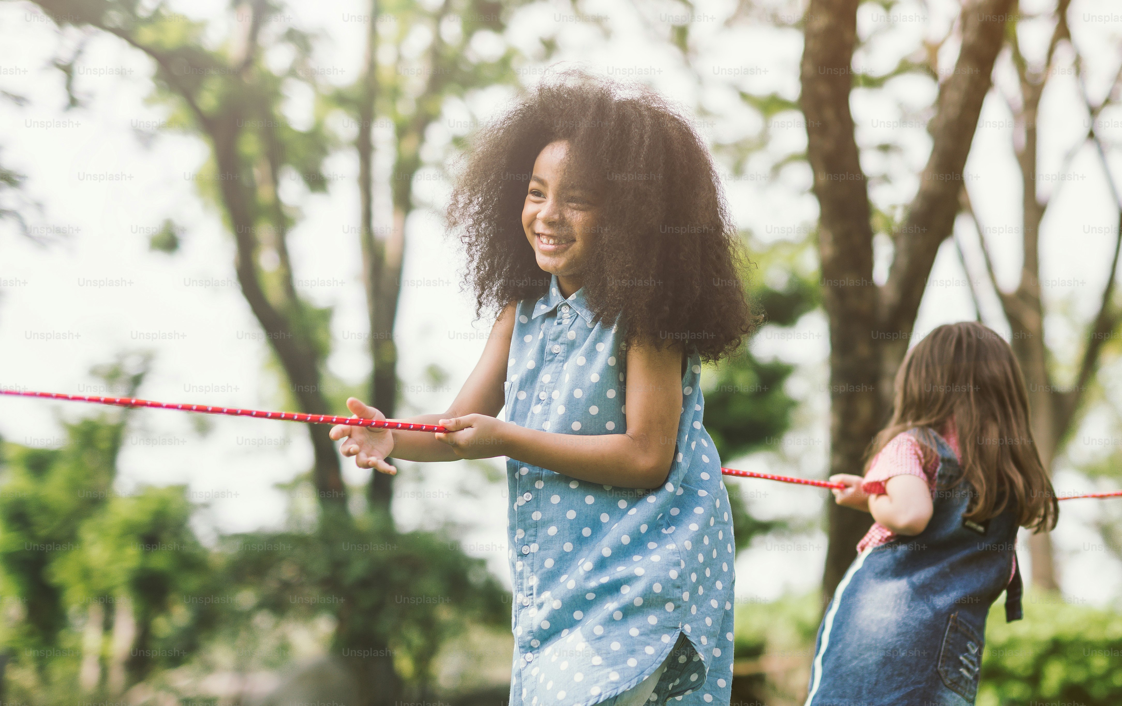 Happy children playing tug of war at the park photo – African-american ...