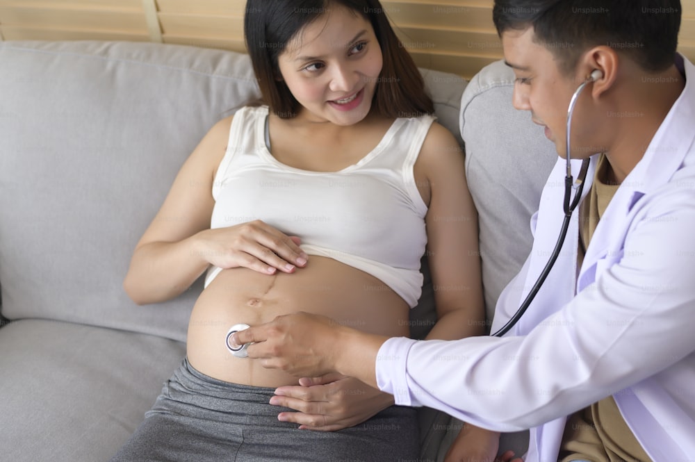 Ein Arzt mit Stethoskop untersucht eine schwangere Frau im Krankenhaus, Gesundheits- und Schwangerschaftsbetreuungskonzept