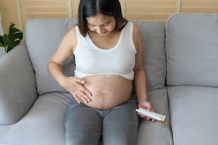 Mulher grávida jovem que aplica creme hidratante na barriga, cuidados de saúde e gravidez