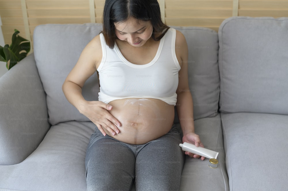 Young pregnant woman applying moisturizing cream on tummy, healthcare and pregnancy care