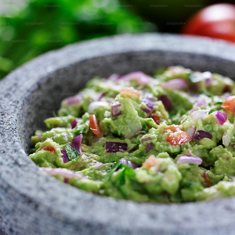 mexican guacamole in stone molcajete close up photo, shot with selective focus. Has onions, tomato, and cilantro