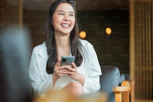 Beautiful young Asian woman use smartphone in coffee shop receive e-mail text good news SME about her client accept contract dealng new project proporsal Young millennial asia woman gesticulate cafe