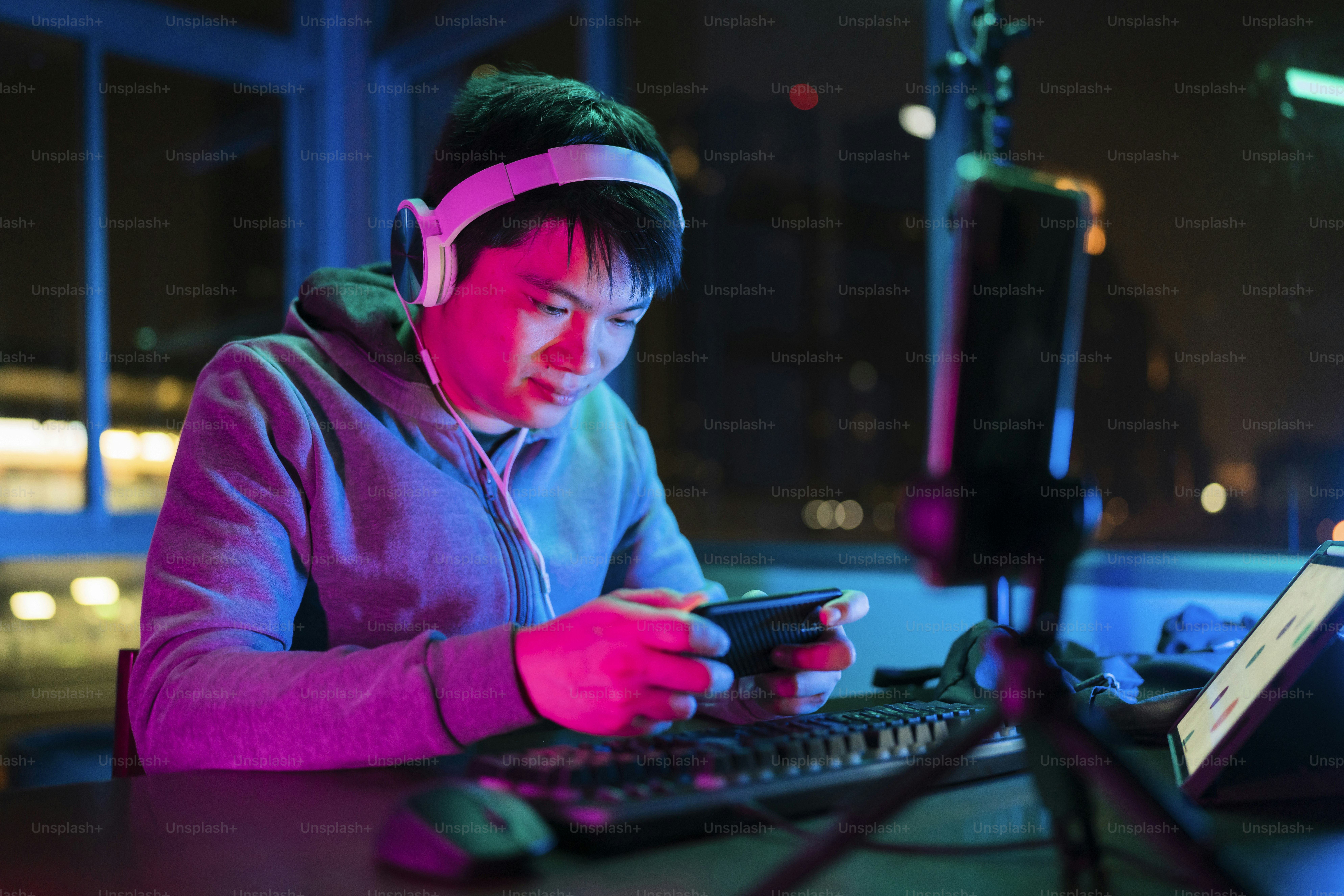 Jugador de deportes electrónicos masculino asiático que juega en línea ligas deportivas juego multijugador a través de un teléfono inteligente con emoción emocionada y alegre, hombre asiático usa auriculares jugando juegos de teléfonos inteligentes en línea junto con amigos