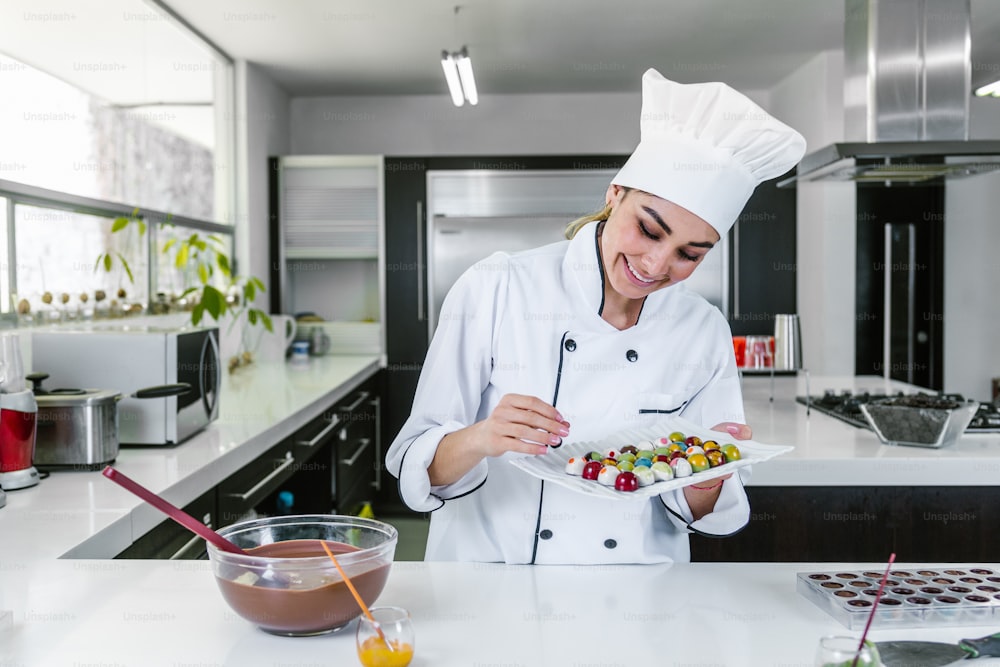 giovane cioccolatiere donna latina in cappello da chef con caramelle di cioccolatini messicani sul piatto in una cucina commerciale in Messico America Latina