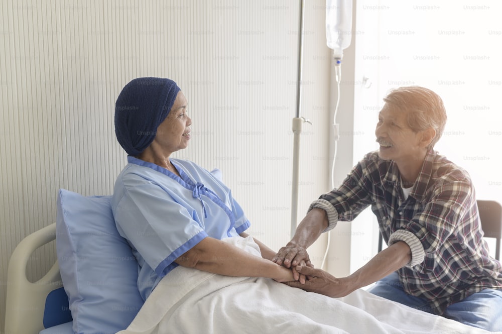 A Senior man visiting cancer patient woman wearing head scarf at hospital, health care and medical concept