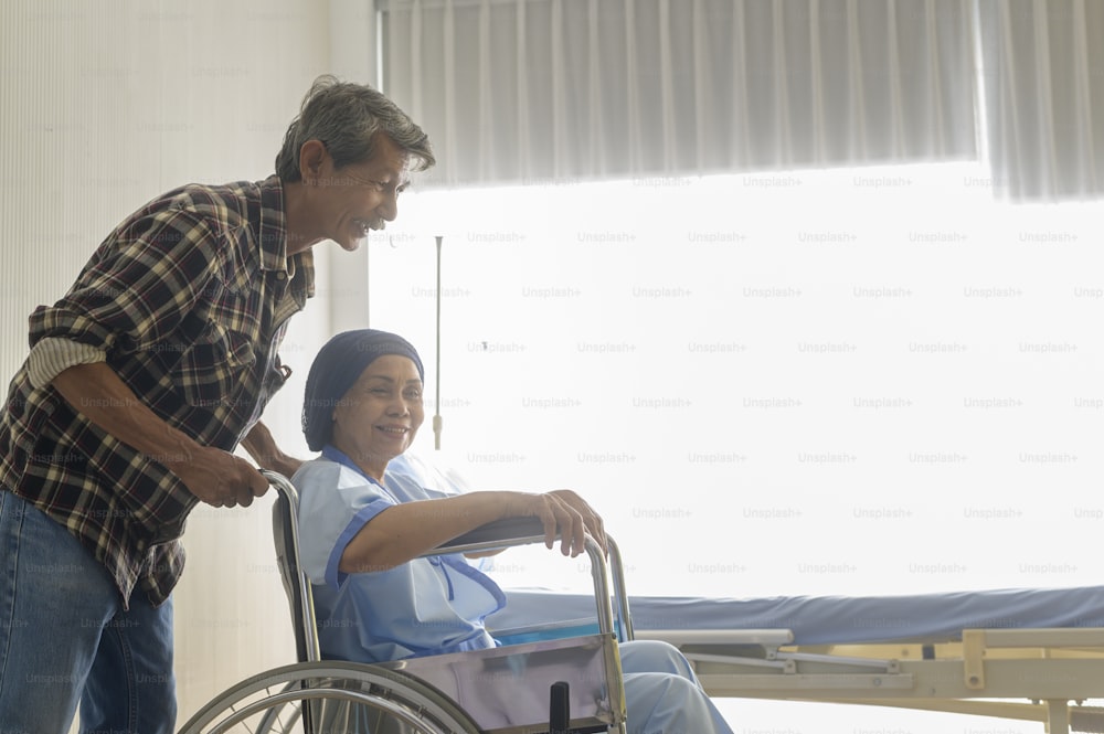 머리 스카프를 두르고 병원, 건강 관리 및 의료 개념에서 휠체어로 이동하는 암 환자 여성을 돕는 노인 남자