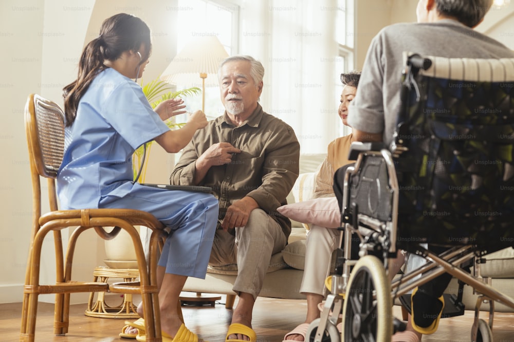 happiness Cheerful elderly woman and men talking with female caregiver nurse doctor having health checking consult at living area,Caretakers with senior couple sitting in living room at nursing home