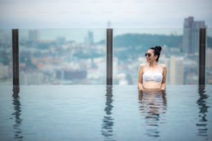 Concepto de viaje asiático. mujer joven disfrutando con la vista del cielo de la ciudad desde la piscina de la azotea del hotel, estilo de vida de la muchacha hermosa al aire libre en tiempo de vacaciones