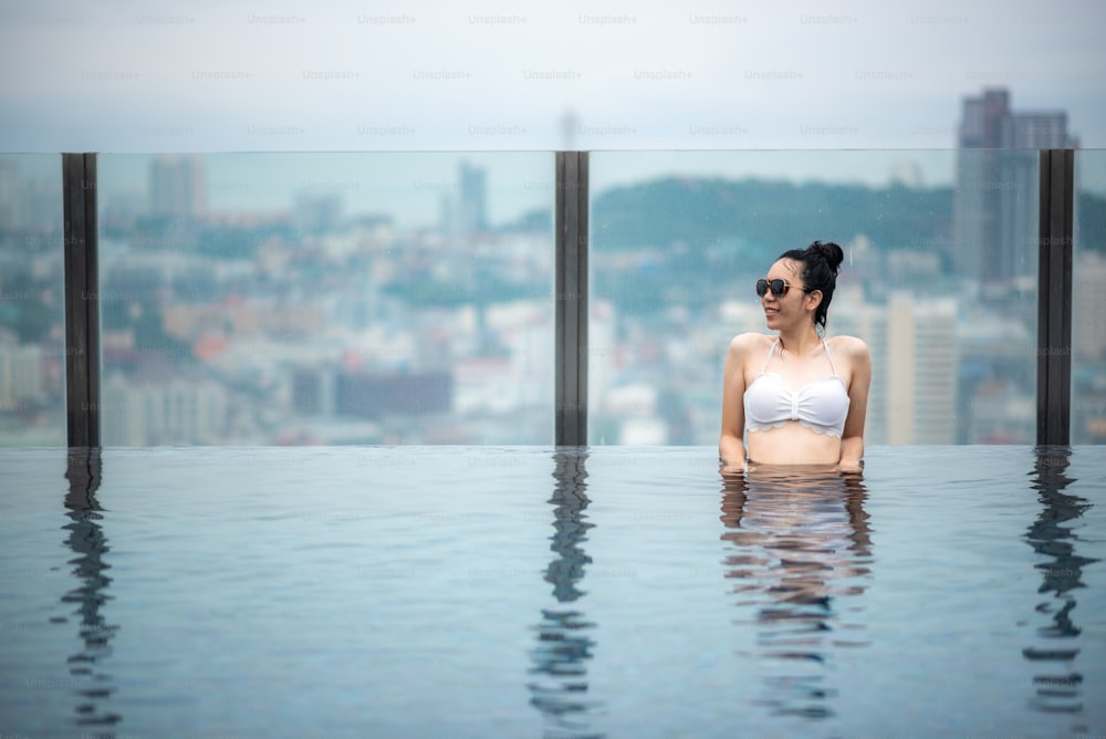 Conceito de viagem asiática. mulher nova que aprecia com a vista do céu da cidade da piscina do telhado do hotel, estilo de vida bonito da menina ao ar livre no tempo de férias