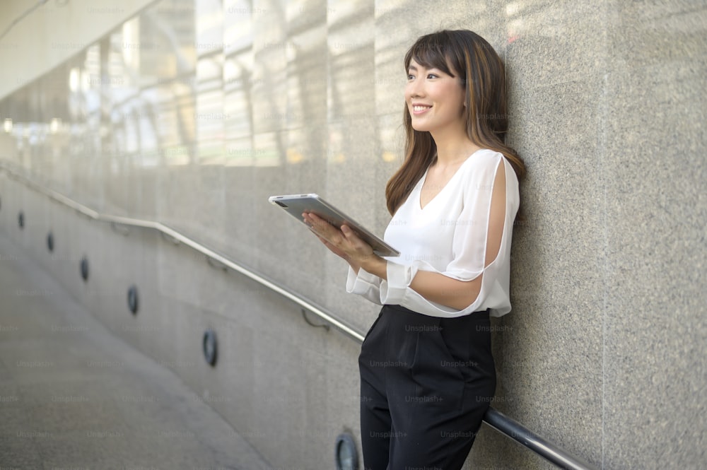 beautiful young asian business woman is using tablet in modern city