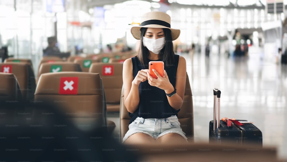 Flughafenterminal Social Distancing Stuhl von Corona-Virus-Pandemie. Junge erwachsene Touristin sitzt mit Maske vor Covid 19 schützen. Menschen reisen mit einem neuen normalen Lebensstilkonzept.