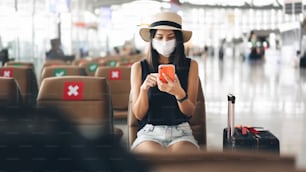 Sedia di distanziamento sociale del terminal aeroportuale da pandemia di virus corona. La giovane donna turista adulta seduta indossa la maschera per proteggersi dal covid 19. Le persone viaggiano con un nuovo concetto di stile di vita normale.