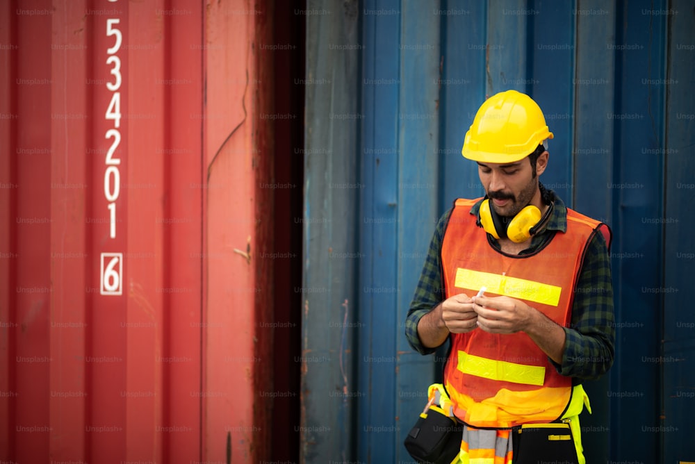 an employee foreman men worker smoking cigarette tobacco nicotine whlie take a break, relax work lifestyle concept, container site, outdoor smoking, men wearing safety vest, helmet and headphone, unhealthy concept