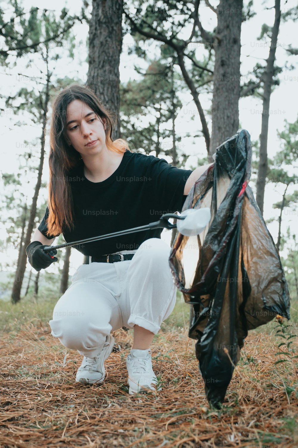 a woman holding a bag of trash in the woods