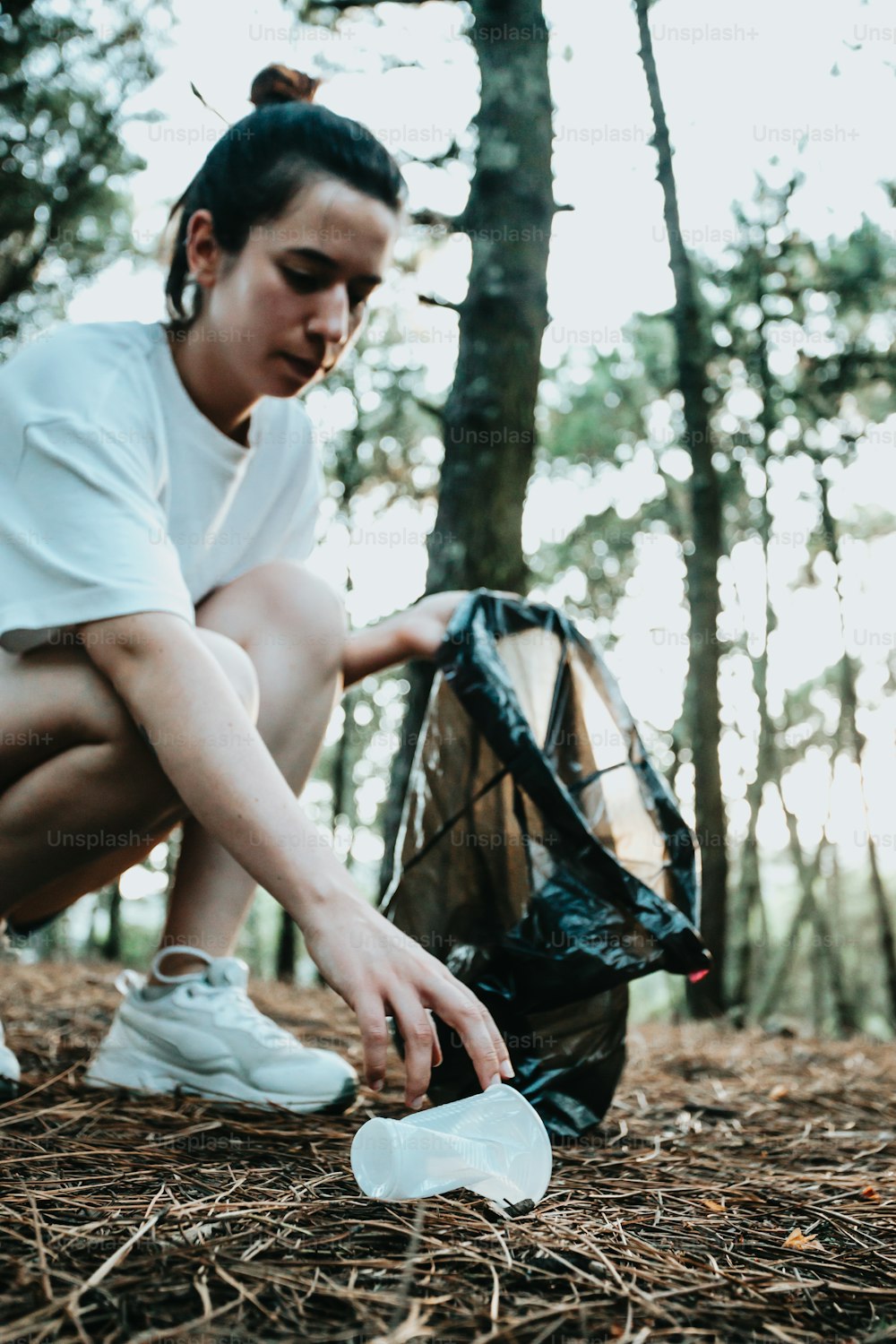 a woman crouches down to pick up a plastic bottle