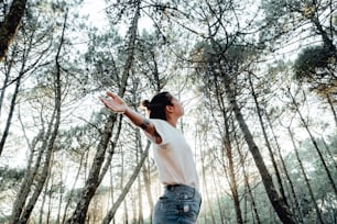 a woman standing in a forest reaching for a frisbee