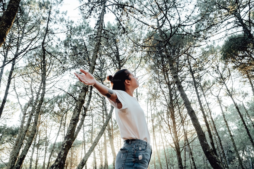 a woman standing in a forest reaching for a frisbee