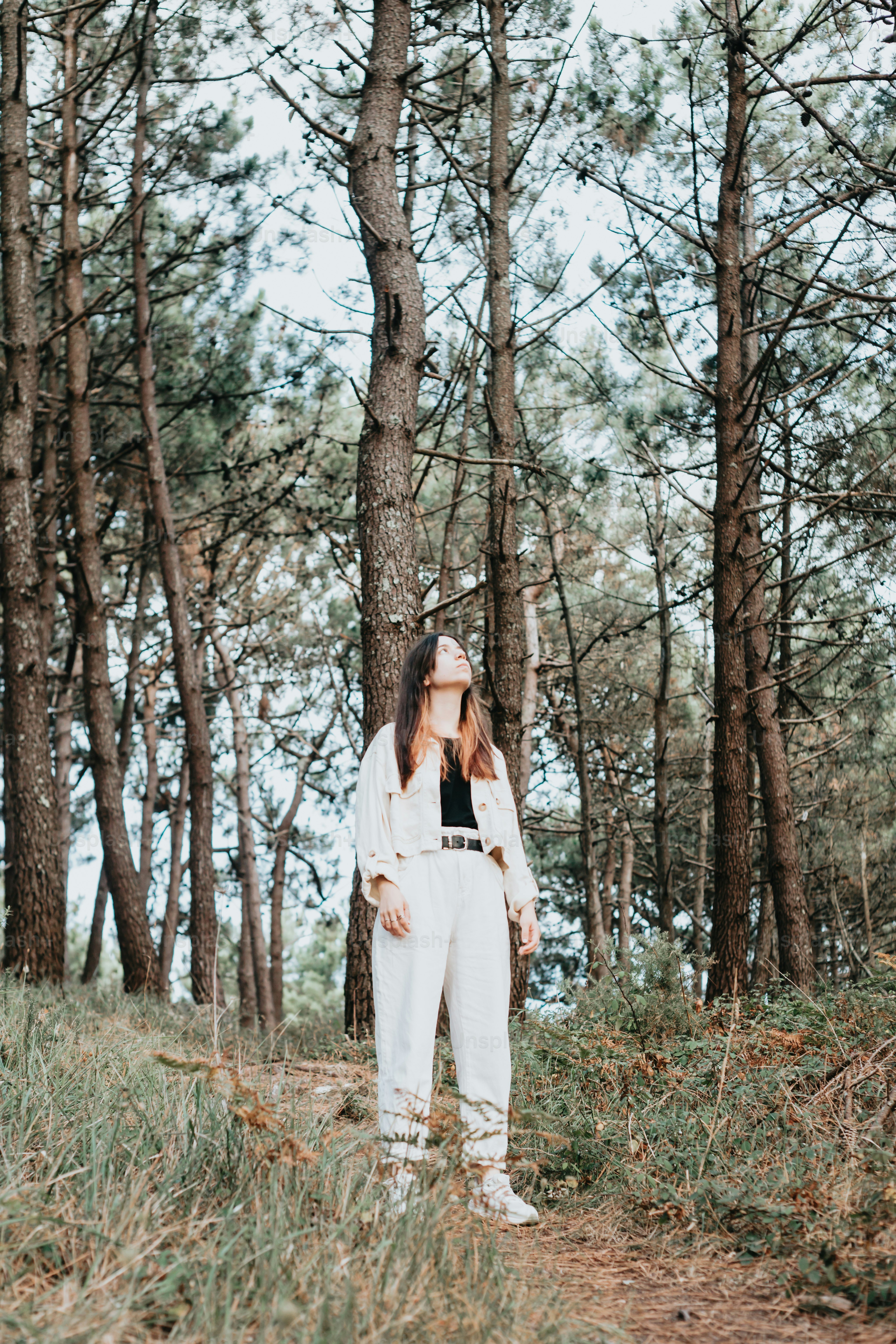 a woman standing in a forest with trees in the background