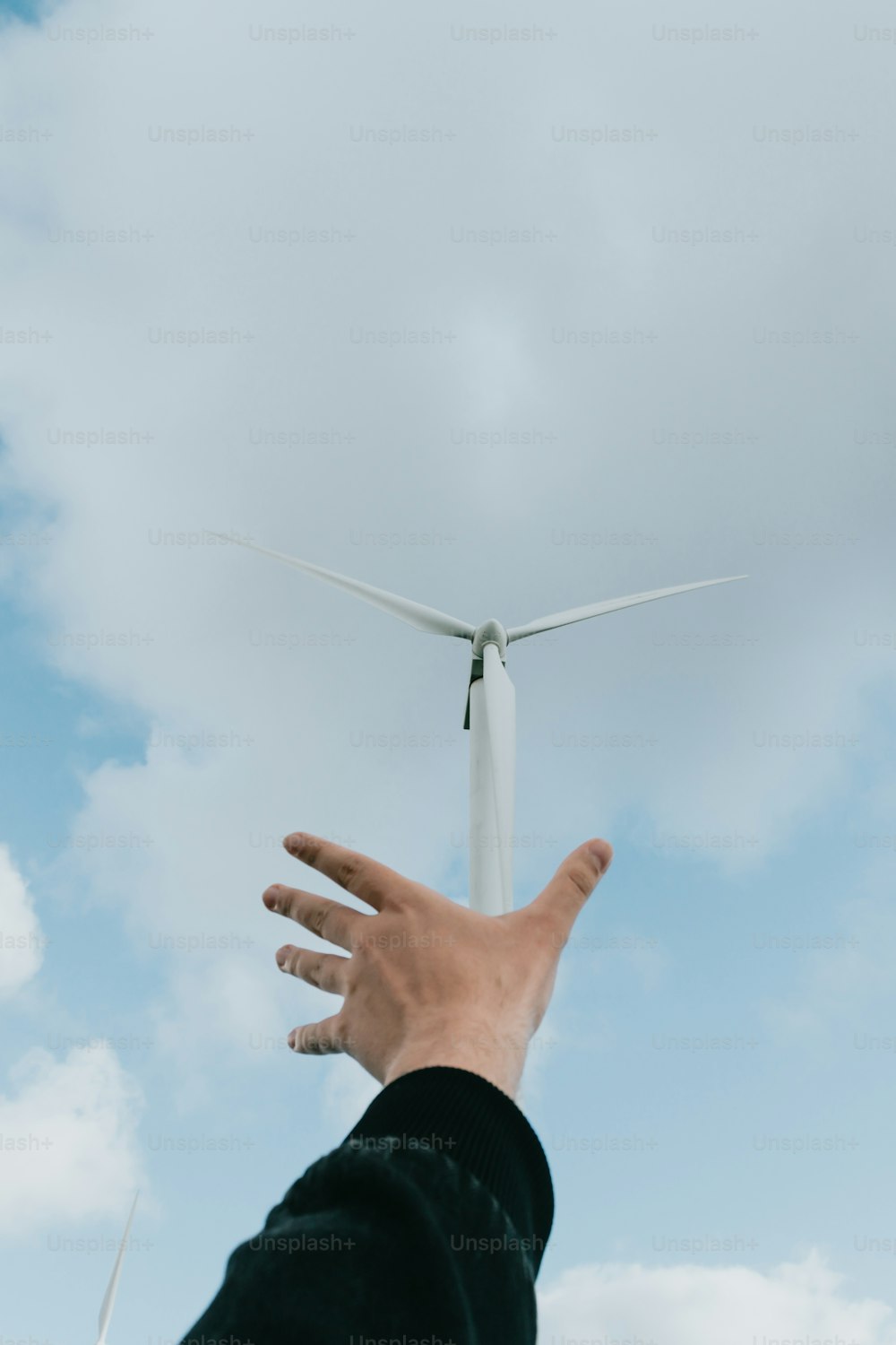 a hand reaching up towards a wind turbine