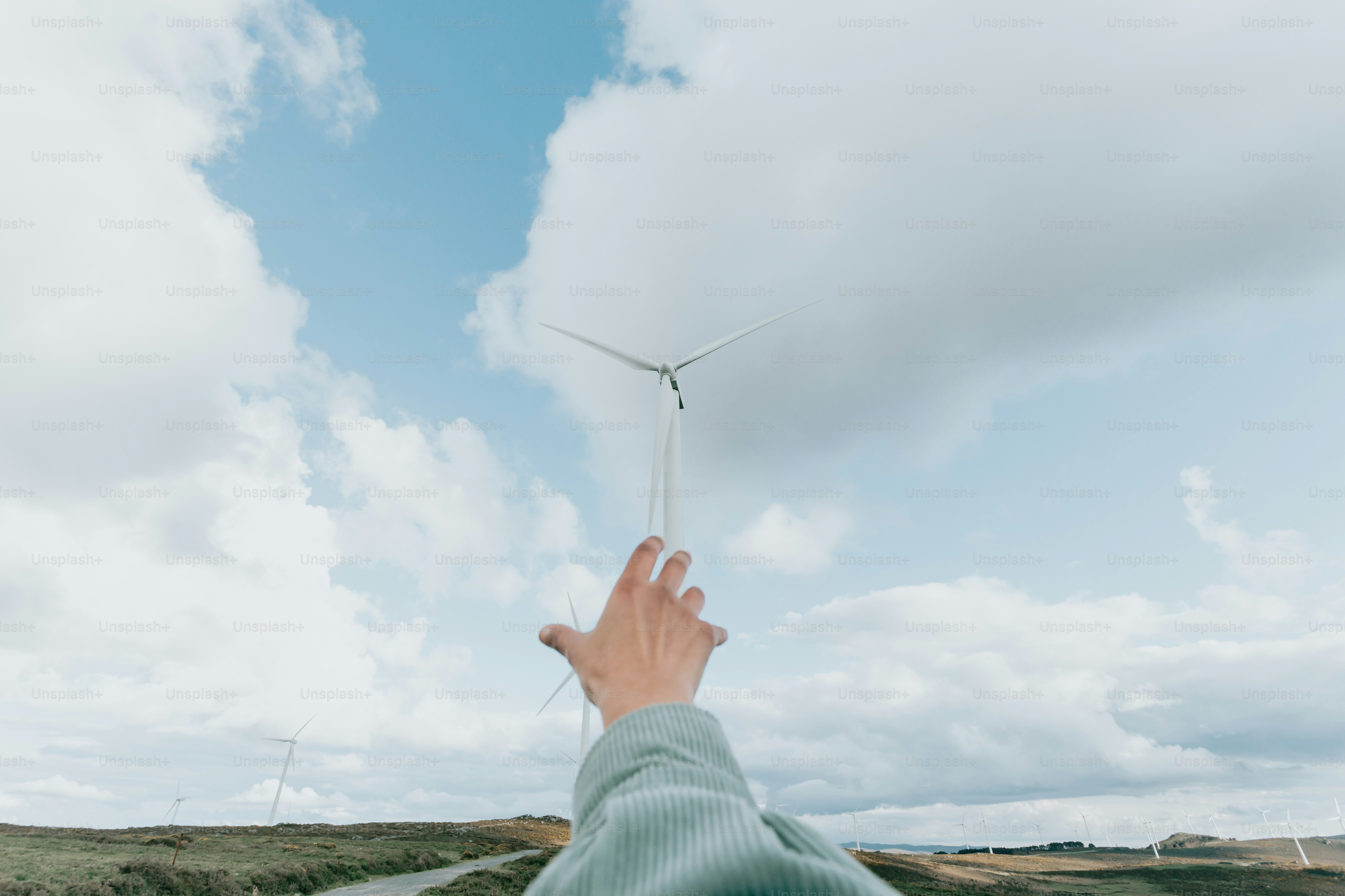a hand reaching up towards a wind turbine