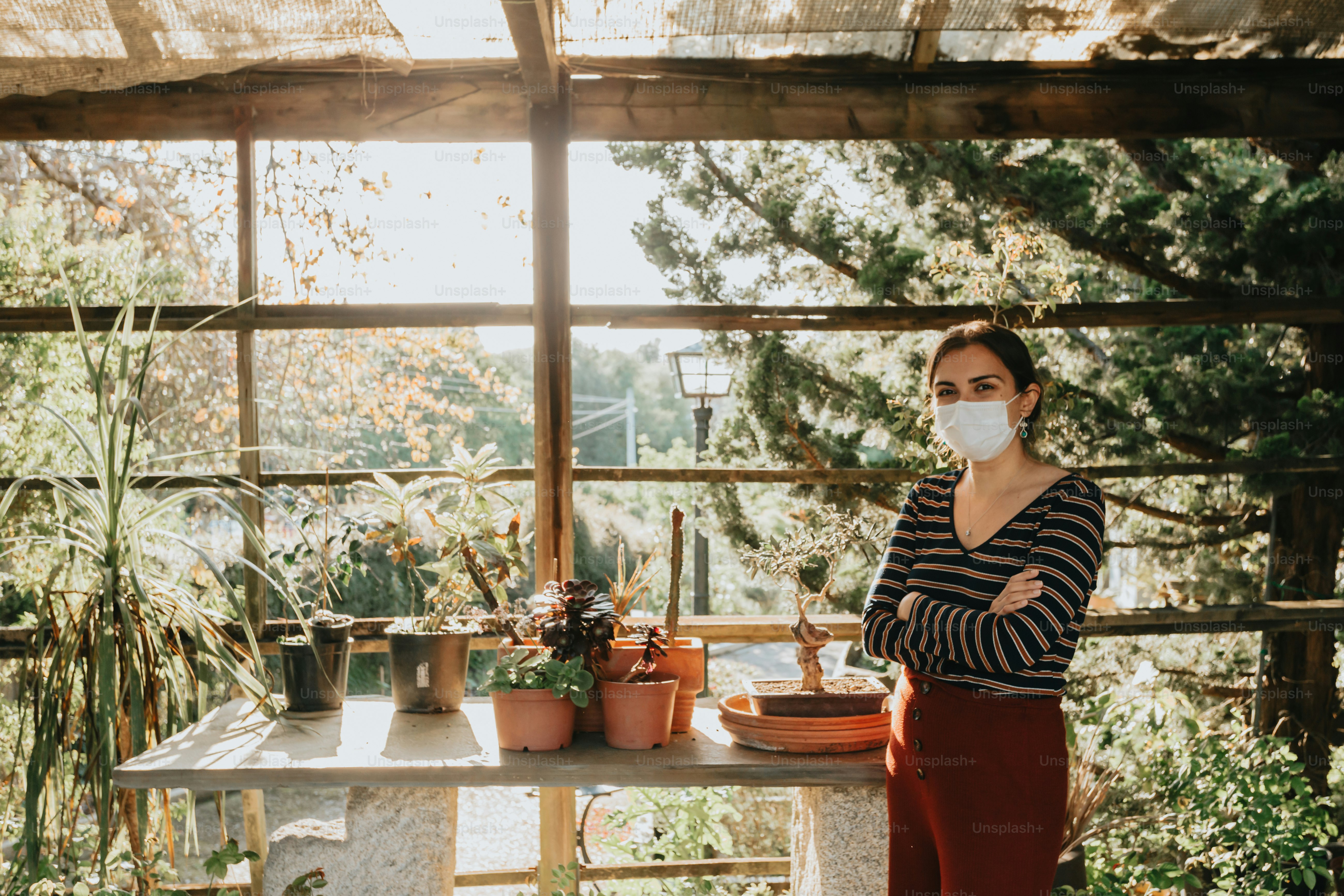 uma mulher usando uma máscara facial em frente a uma mesa com vasos de plantas