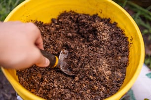 a person scooping dirt into a yellow bowl