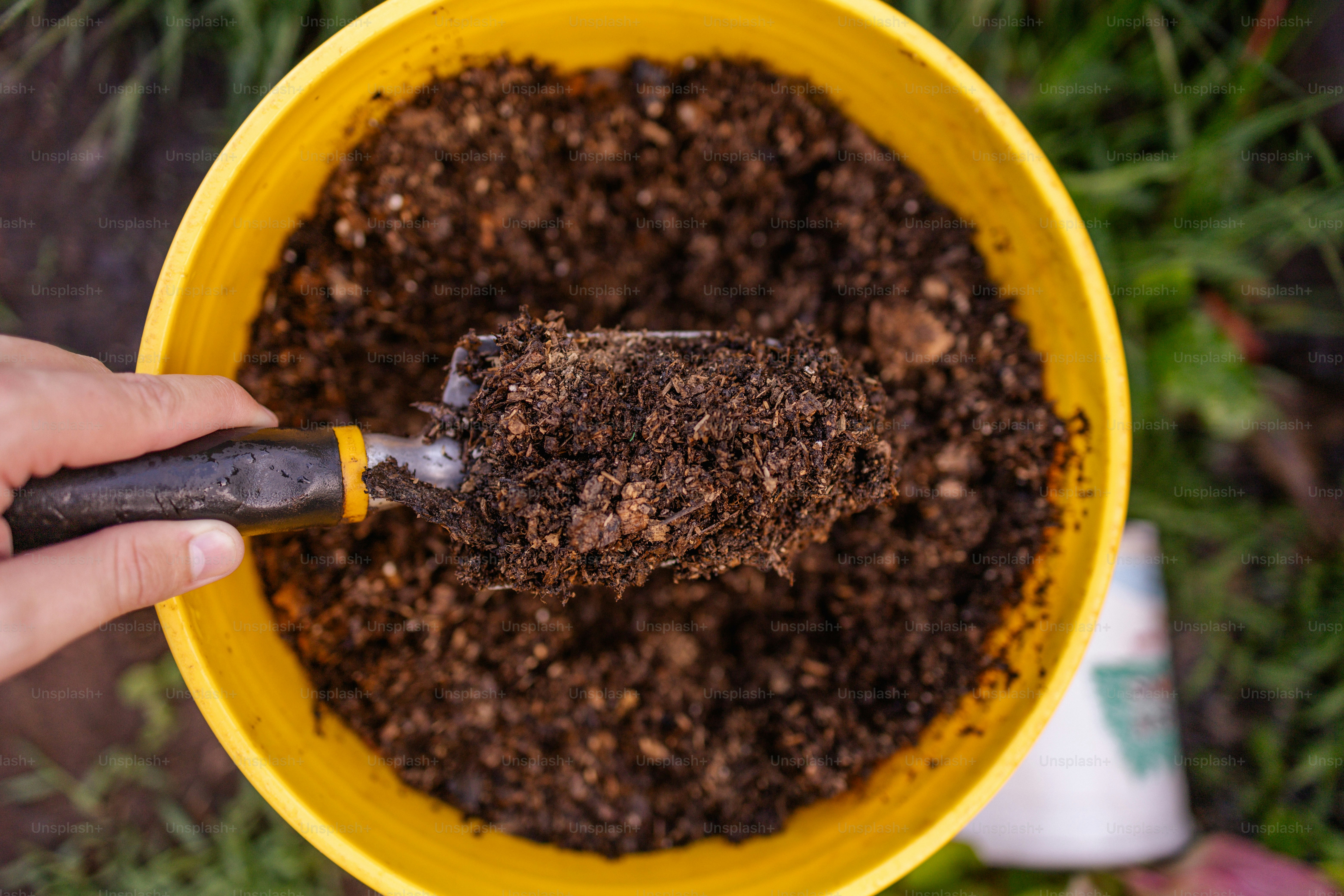 a person scooping dirt into a yellow bowl