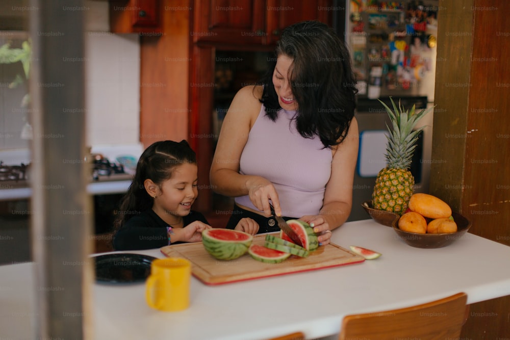 a woman and a little girl cutting watermelon on a cutting board