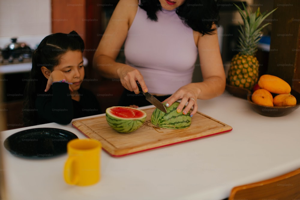 a woman cutting up a watermelon on a cutting board