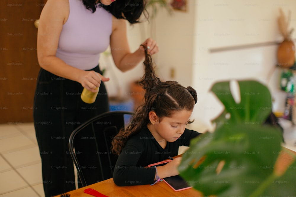 uma mulher penteando o cabelo de uma garotinha enquanto está sentada em uma mesa