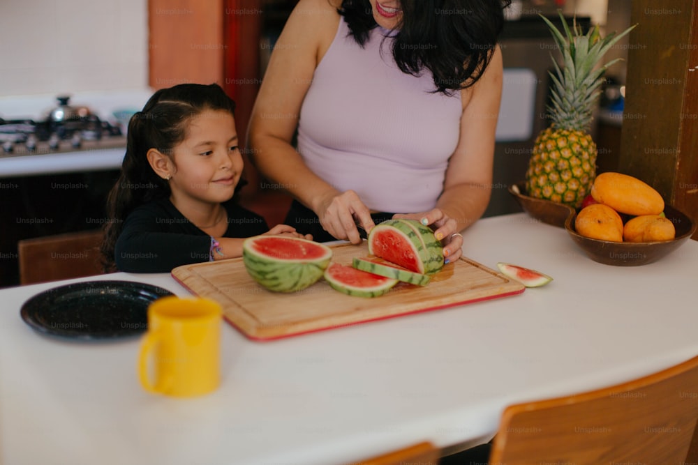 uma mulher e uma menina cortando melancia em uma tábua de corte