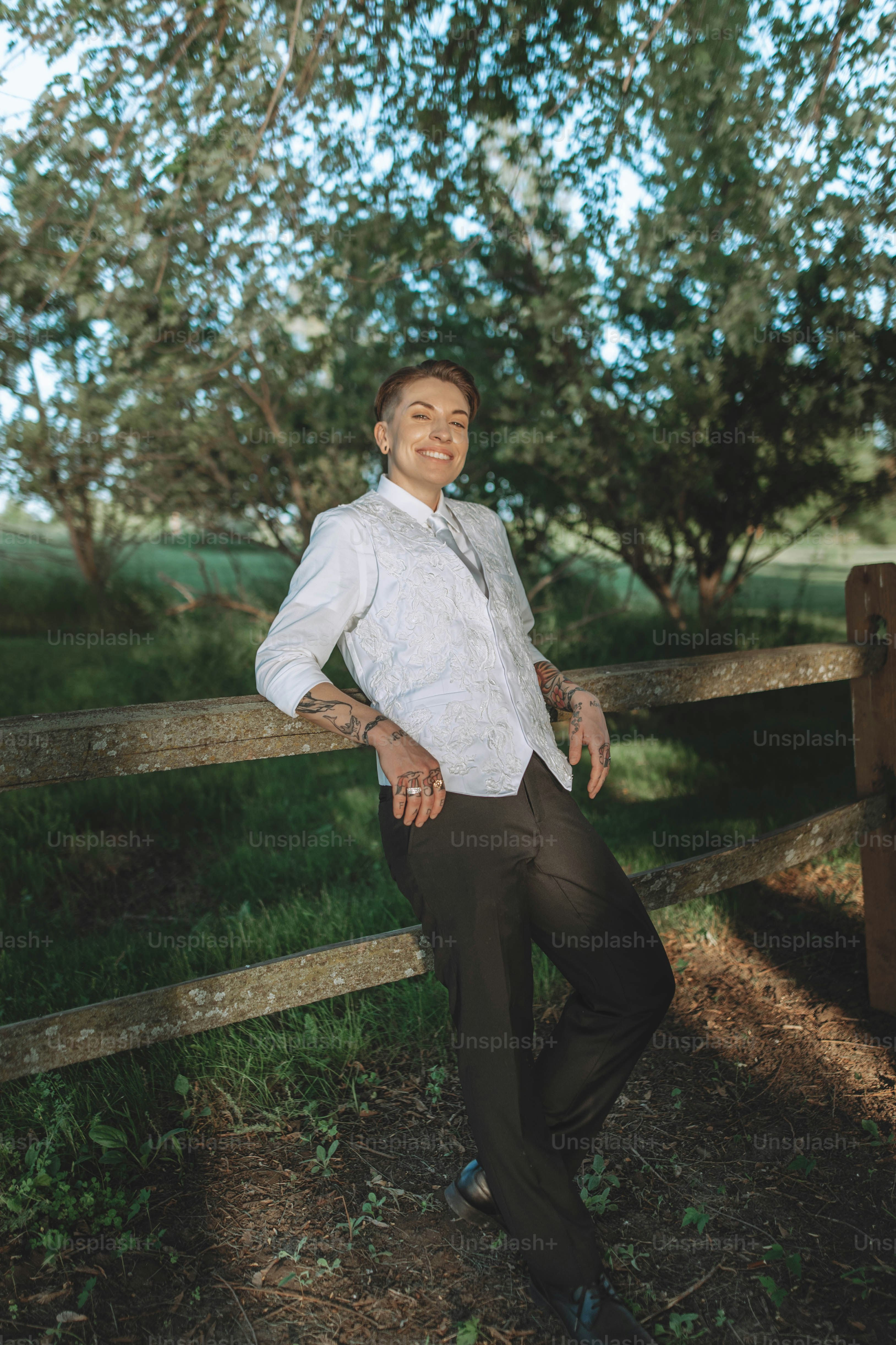 a man in a white shirt and black pants leaning on a fence