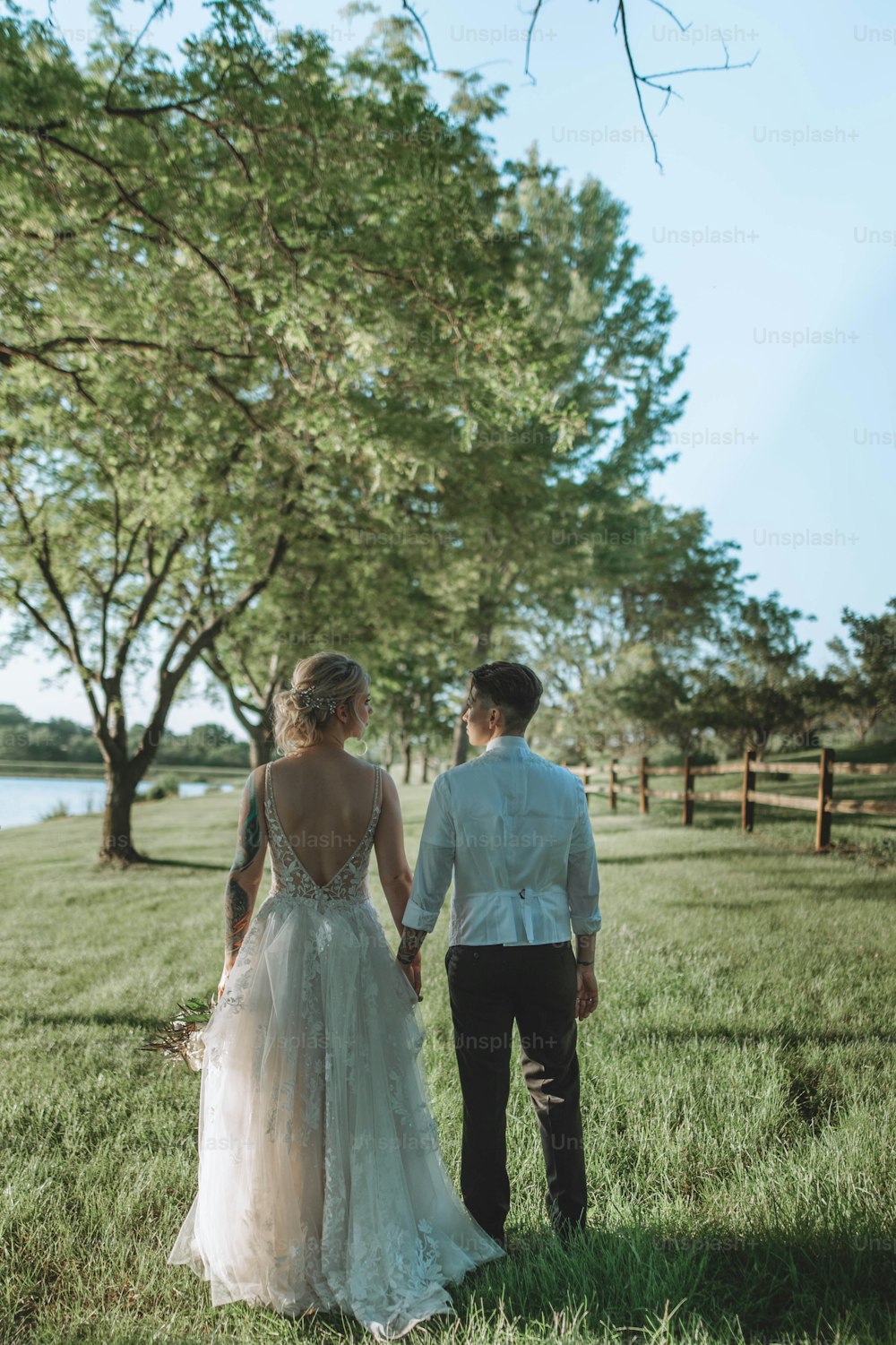 a bride and groom holding hands walking through a field