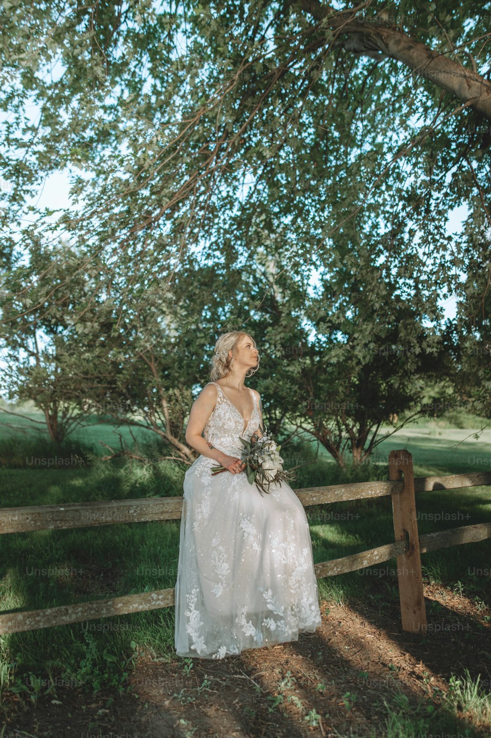a woman in a wedding dress sitting on a fence