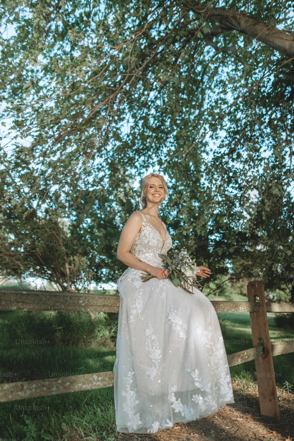 a woman in a wedding dress sitting on a fence