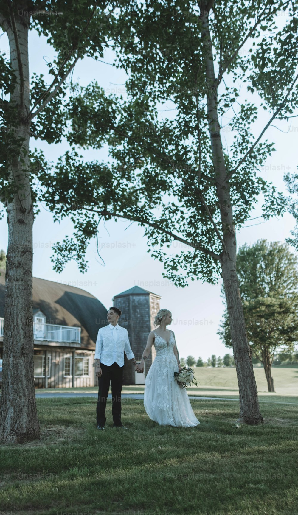 a bride and groom standing in the grass under some trees