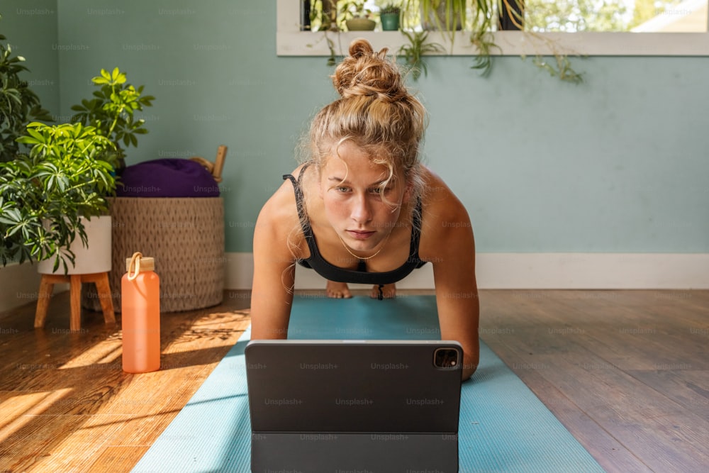Una mujer en una esterilla de yoga usando una computadora portátil