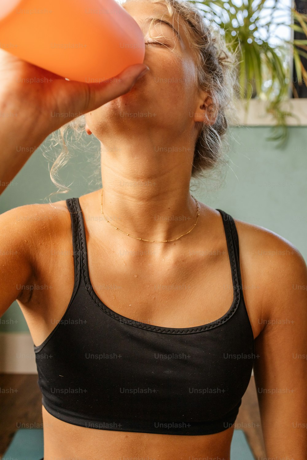 Una mujer con un sostén deportivo bebiendo de una taza naranja
