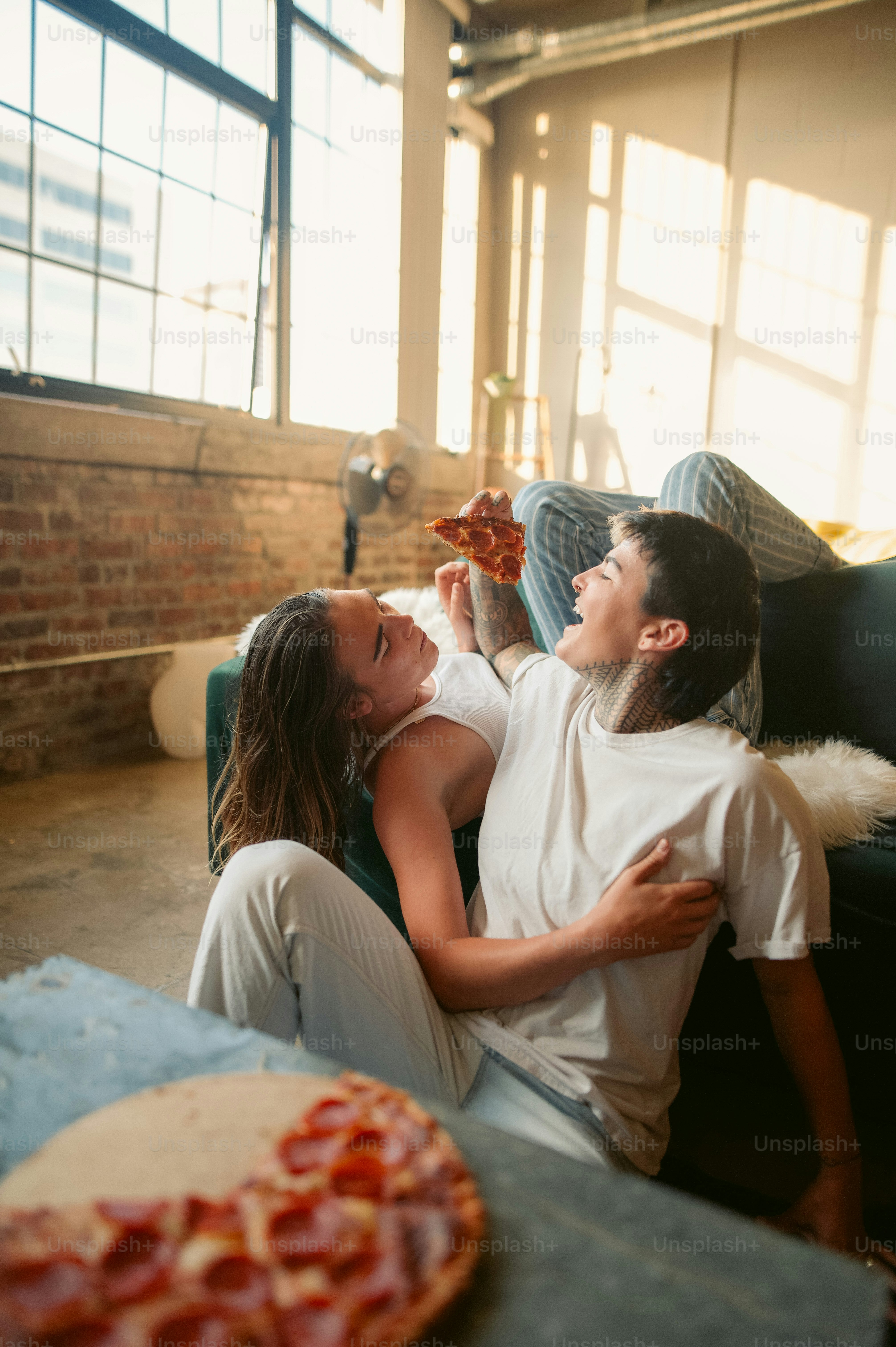 Un uomo e una donna seduti su un divano che mangiano pizza