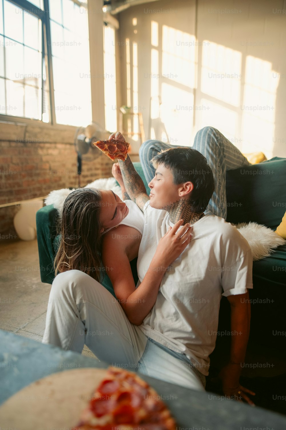 a boy and a girl sitting on a couch eating pizza